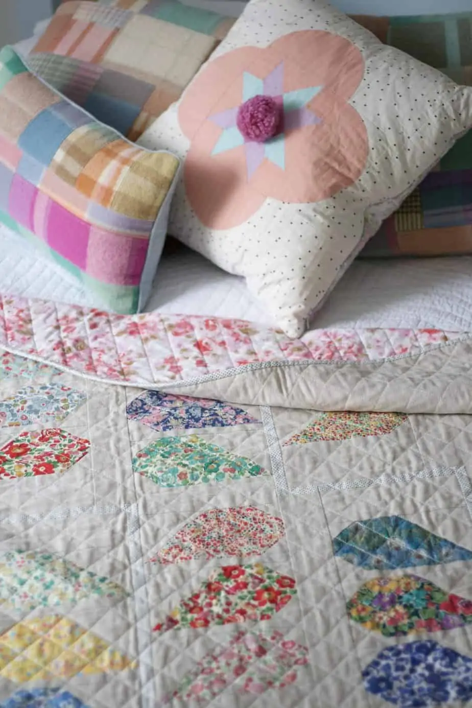 Close up of quilt featuring Liberty prints on blue bed with scatter cushions in background.