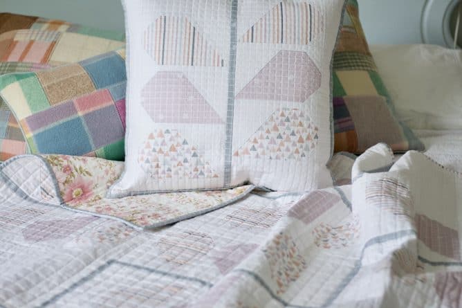 Close up of cushion and quilt featuring plant design in soft pinks and neutrals with colourful scatter cushions in background.