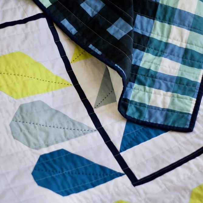 Close up of quilt with plant design with gingham backing showing.